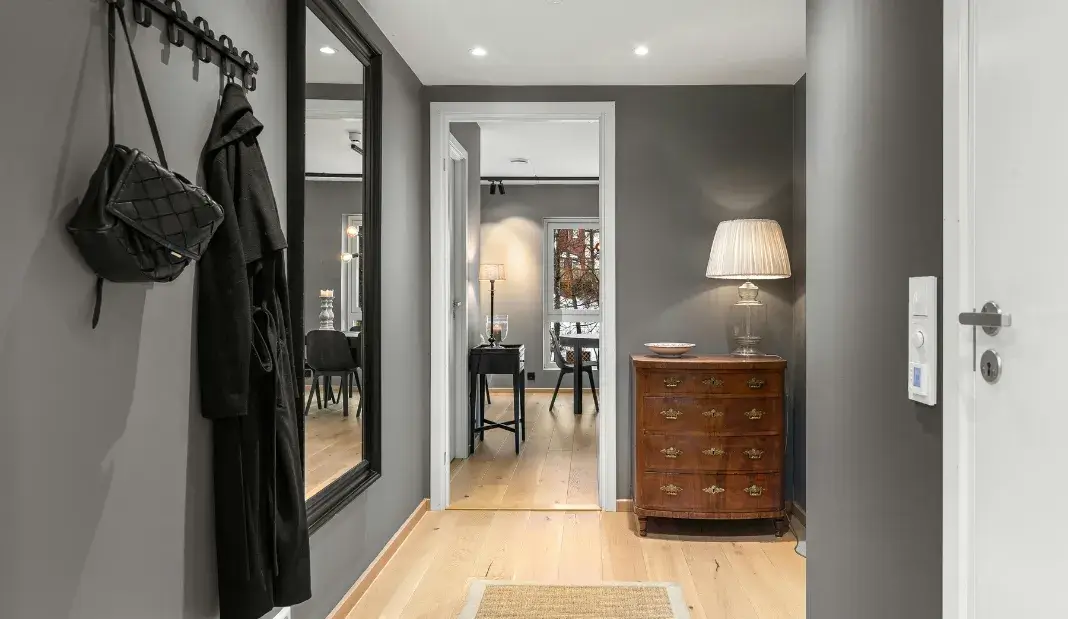Clean and organized hallway with coat hooks, mirror, and wooden flooring.