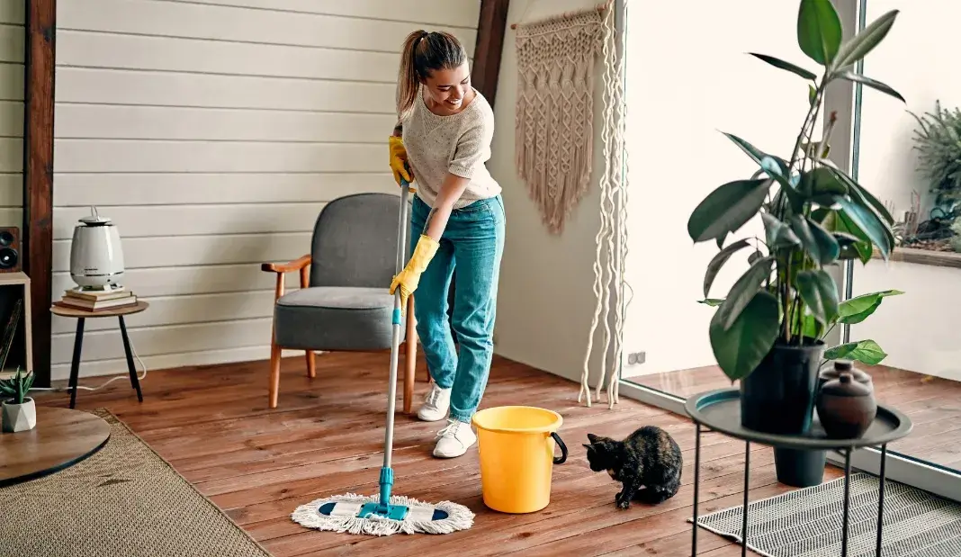 Woman mopping a wood floor with gloves and cleaning tools, demonstrating practical holiday cleaning tips.